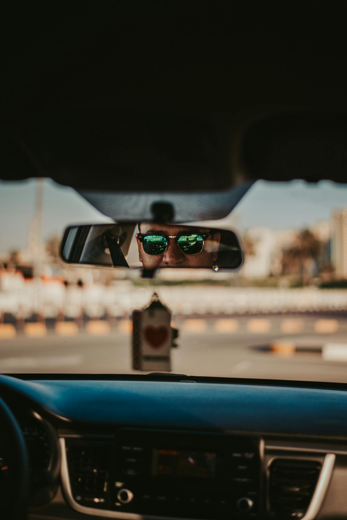 Urban driving with man's reflection in rearview mirror, cityscape visible.